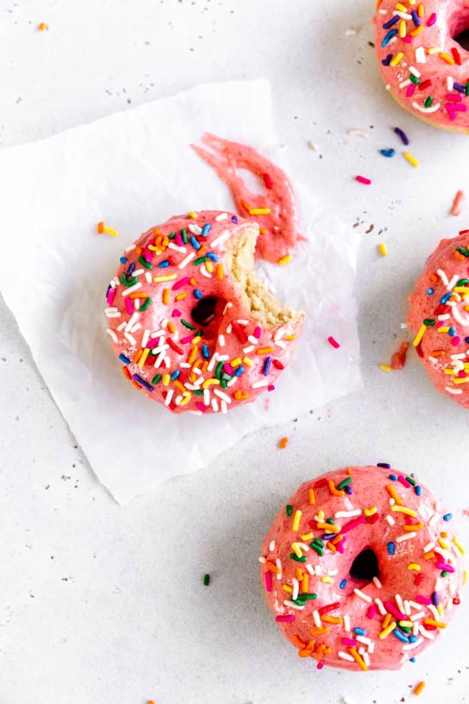 Baked, frosted donut on on a sheet of wax paper smeared in frosted.