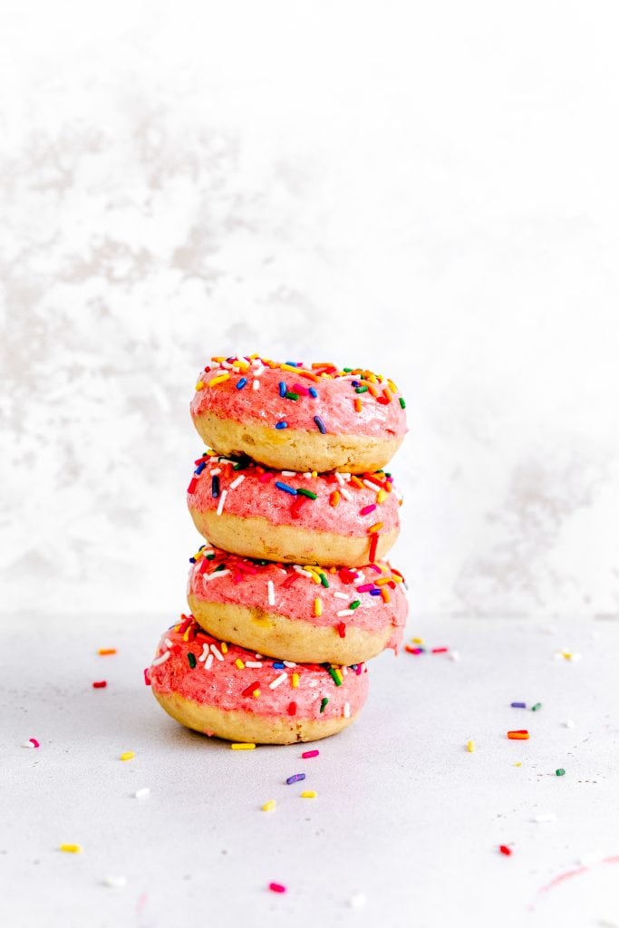 Stack of baked donuts topped with pink icing and multicolored sprinkles.