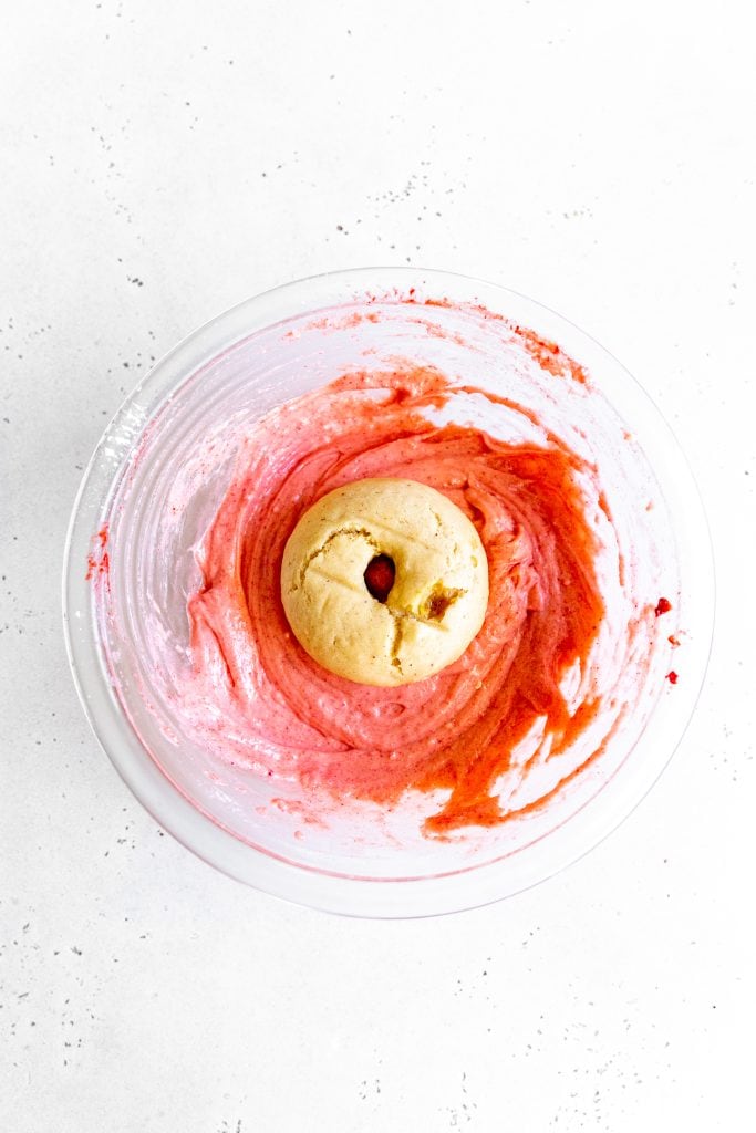 Baked vegan donut facedown in a bowl of pink icing.