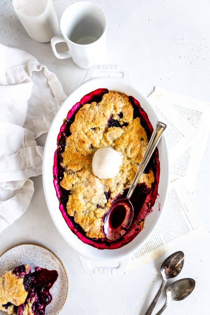 Spoon digging into blackberry cobbler baking dish.