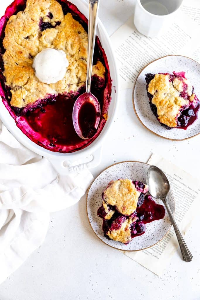 Blackberry cobbler on two white serving plates next to a dish of cobbler.