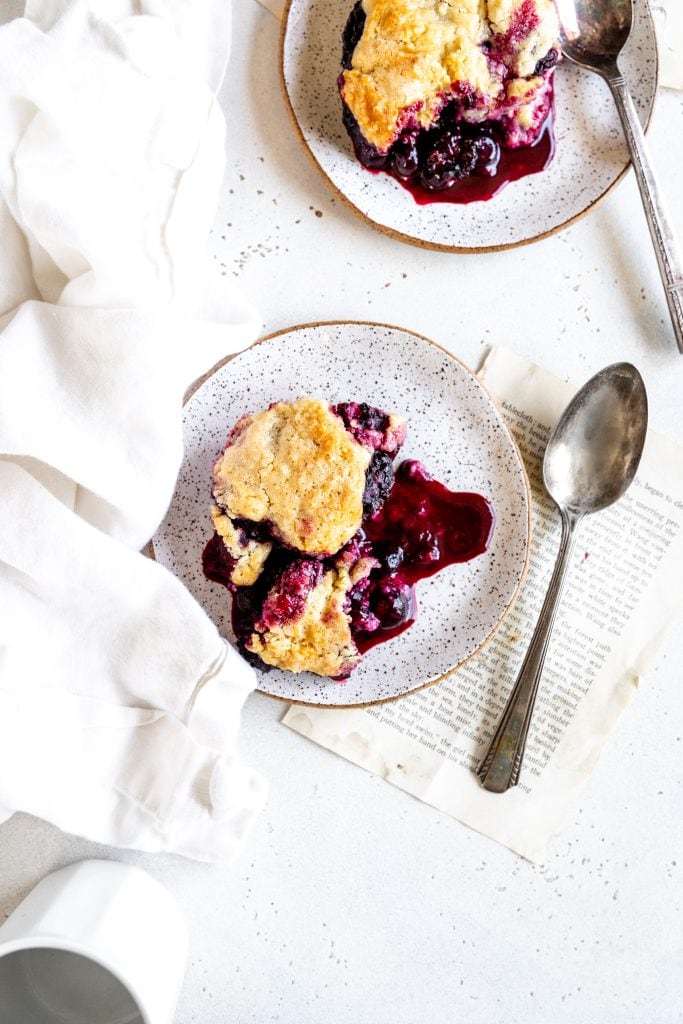 Two plates of blackberry cobbler with spoons and a white mug.