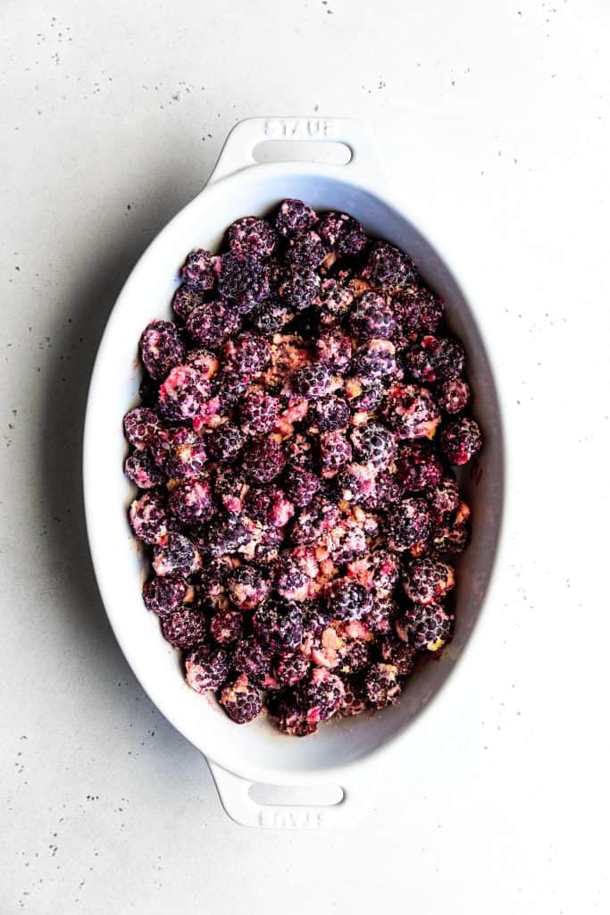 Unbaked blackberry cobbler filling in a white oval baking dish.