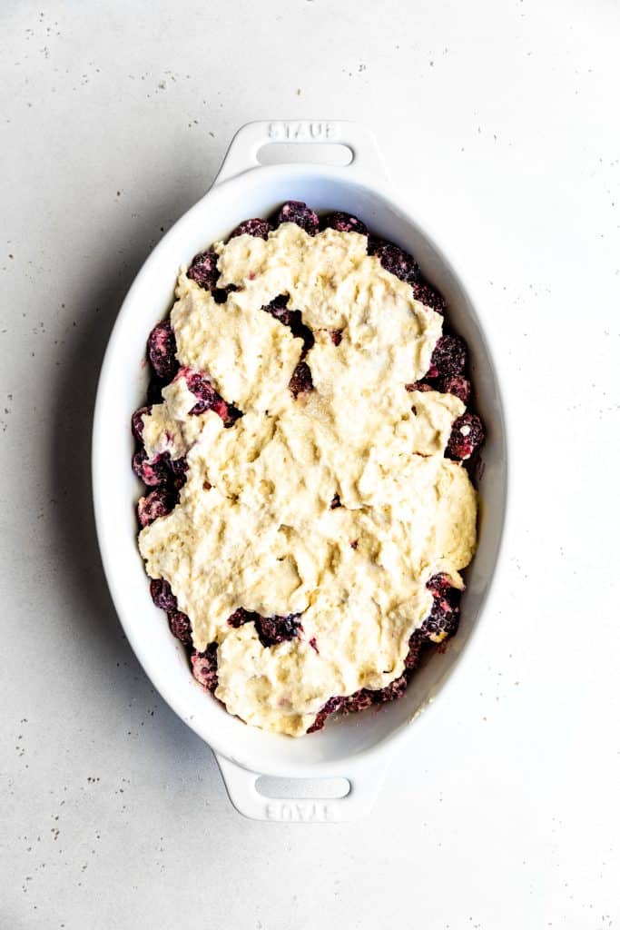 Unbaked blackberry cobbler in a white oval baking dish.