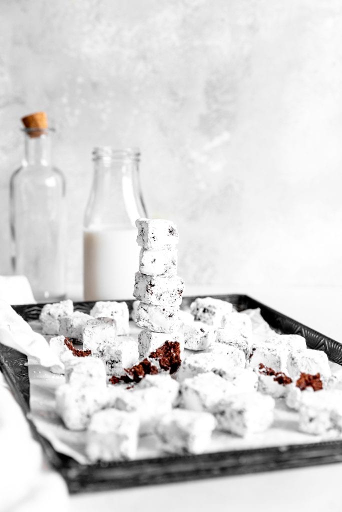 Stack of brownie bites on a baking sheet in front of a jug of milk.