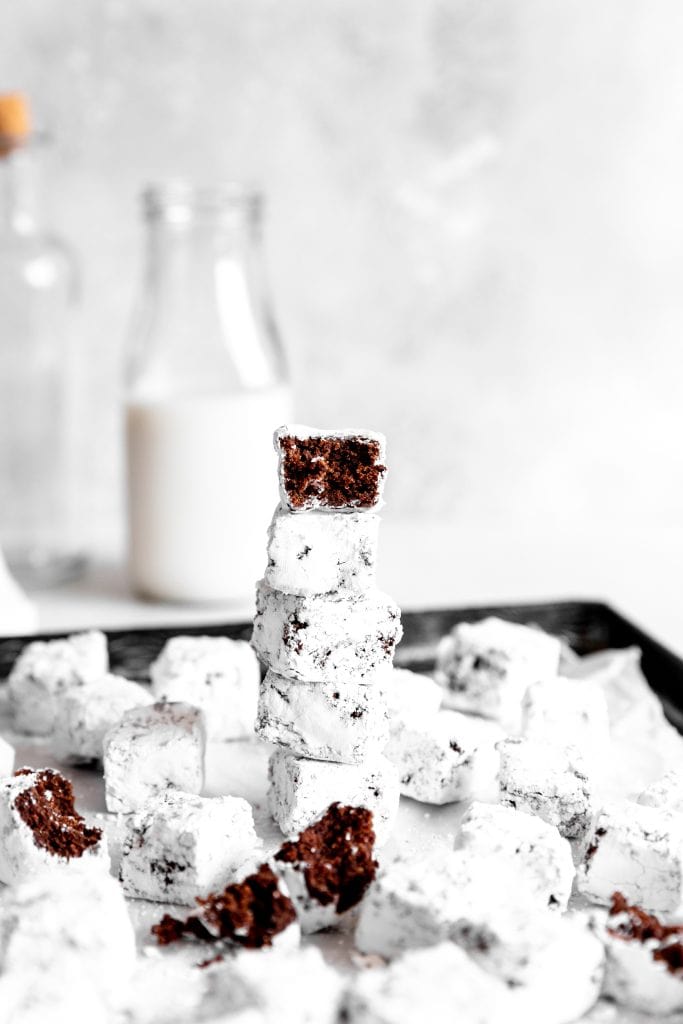 Brownie bite with a bite taken out of it on top of a stack of brownie bites in front of a jug of milk.