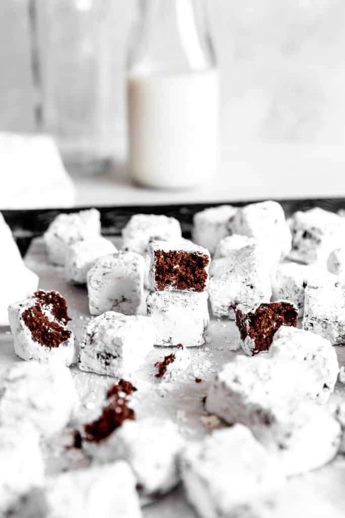 Brownie bite with a bite taken out of it on a baking sheet in front of a jug of milk.