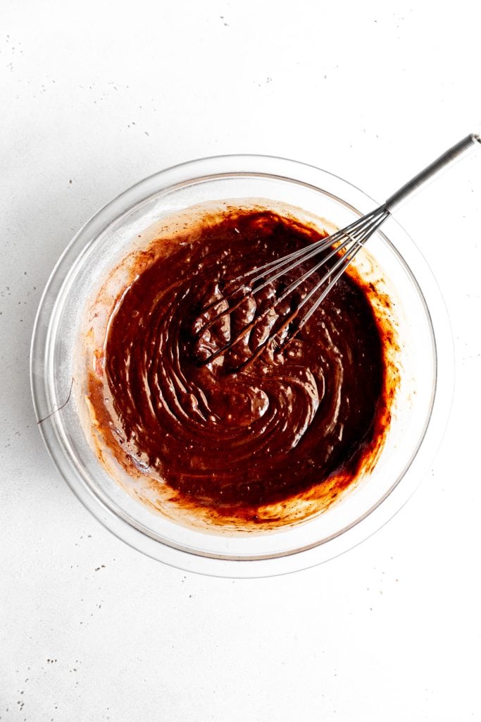 Glass bowl filled with brownie batter and a whisk.