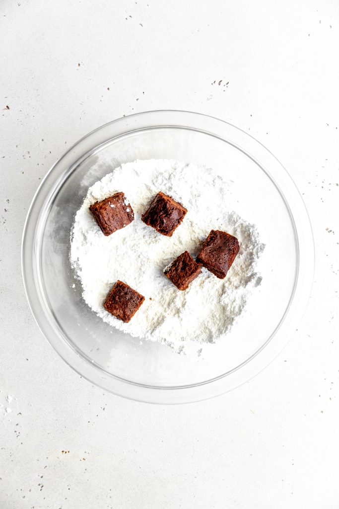 Brownie bites in a glass bowl of powdered sugar.