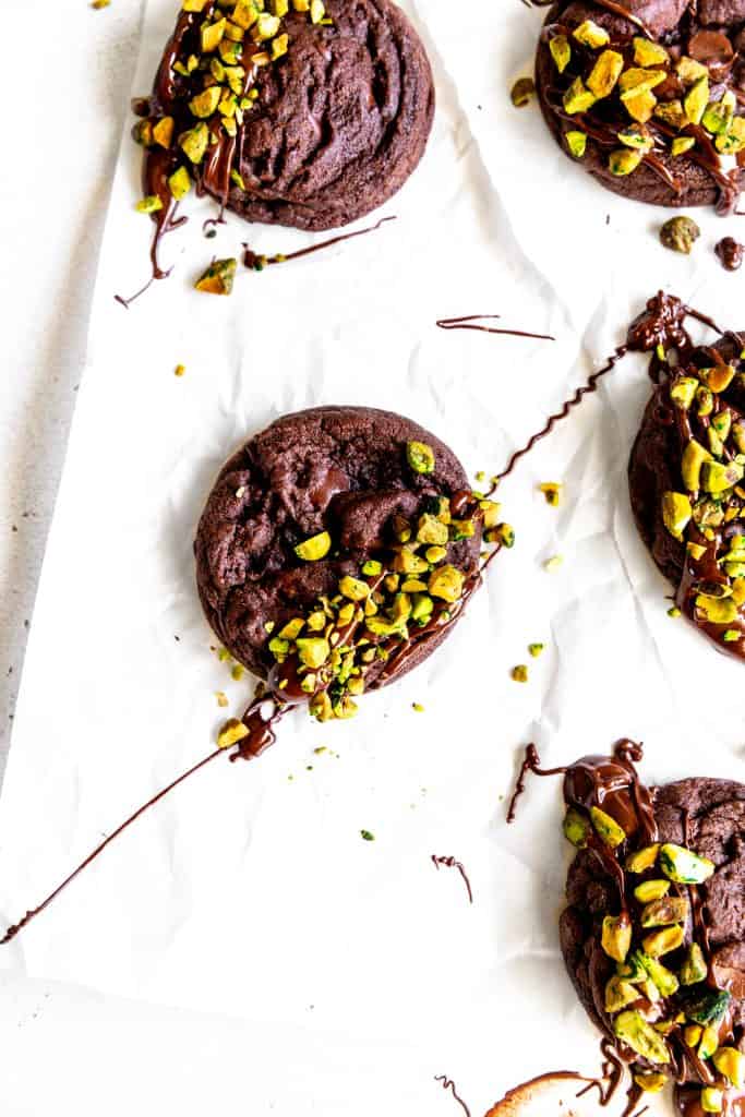 Chocolate pistachio cookie drizzled in chocolate on a white surface.