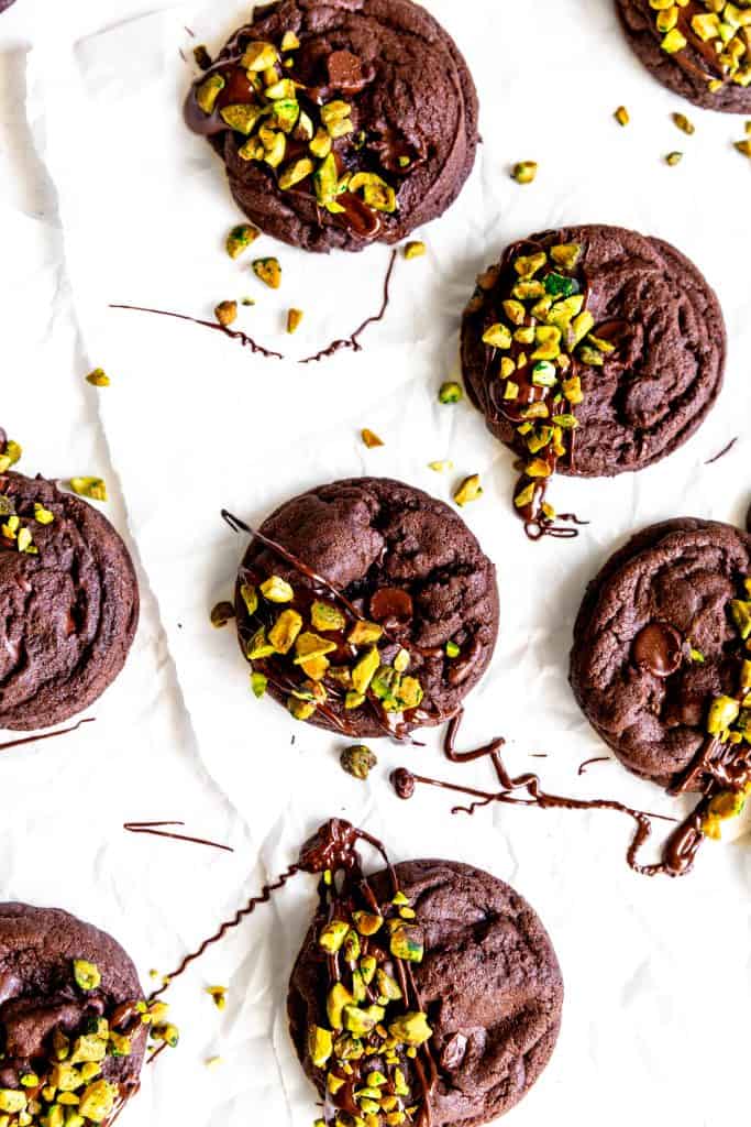 Chocolate pistachio cookies drizzled in chocolate on a white background.