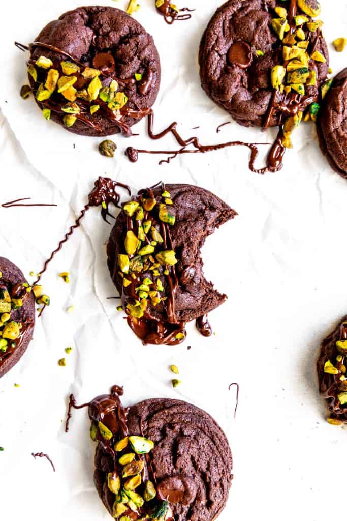 Chocolate pistachio cookie with a bite taken out of it surrounded by more cookies.