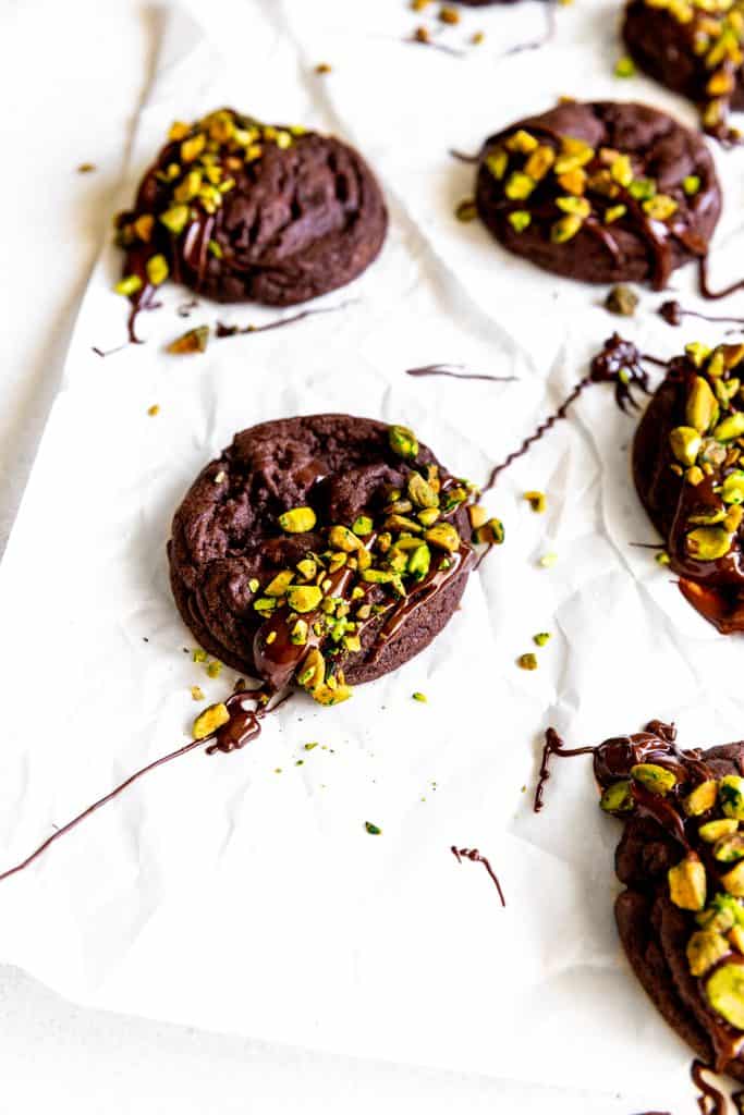 Chocolate pistachio cookie drizzled in chocolate over a piece of parchment paper.