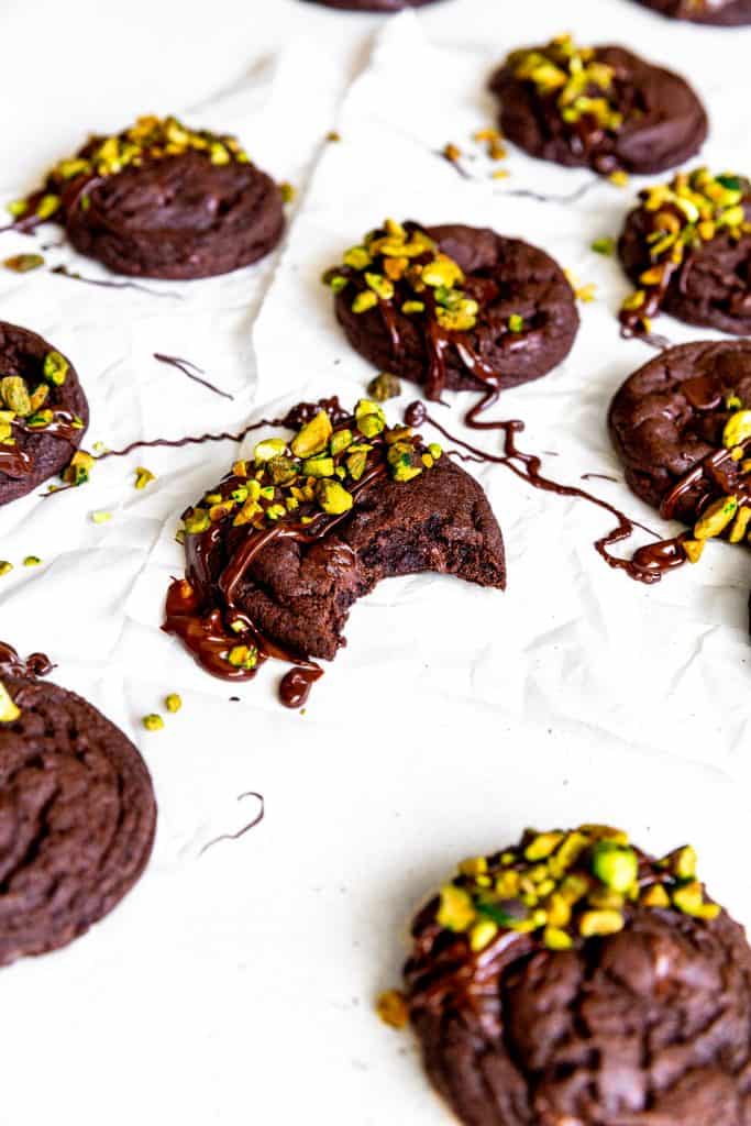 Chocolate pistachio cookie with a bite taken out of it on a white surface.