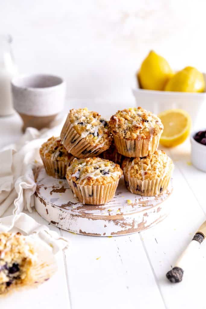 Pile of lemon blueberry muffins in front of fresh lemons and a jug of milk.