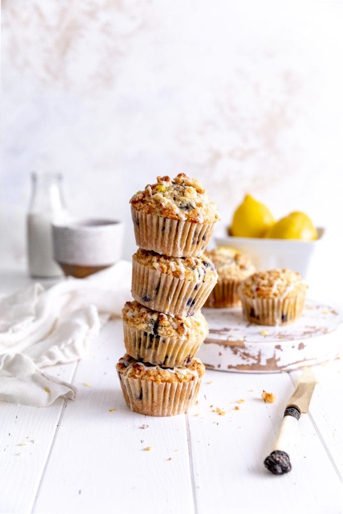 Stack of lemon blueberry muffins in front of a bowl of lemons and a jug of milk.