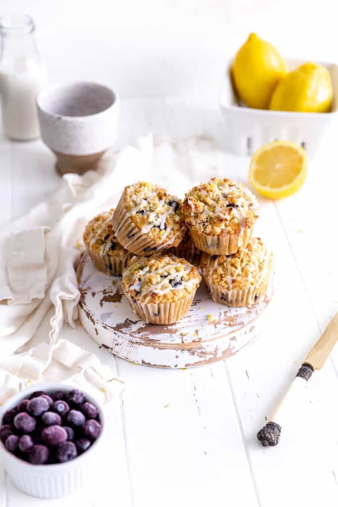 Pile of lemon blueberry muffins in front of fresh lemons and a jug of milk.