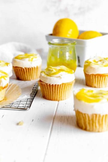 Vegan lemon cupcakes, a basket of lemons and a jar of lemon curd.