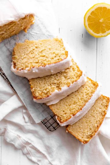 Four slices of lemon loaf laid on a wire cooling rack and half a lemon.
