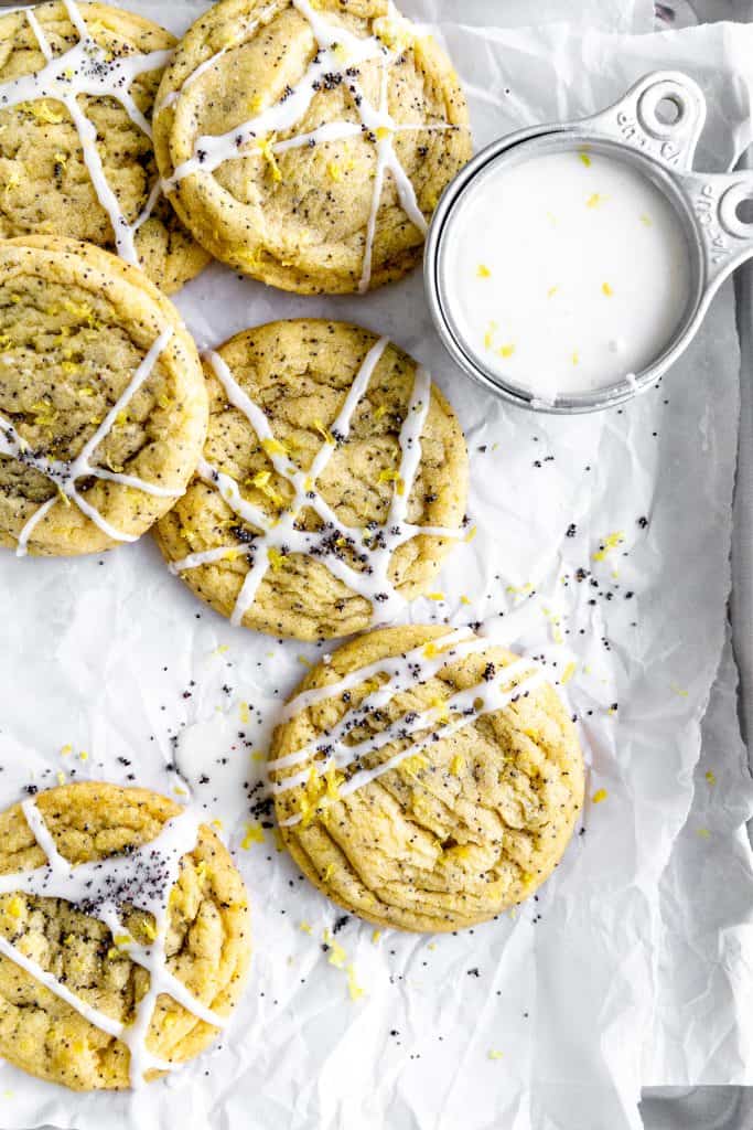 Lemon poppyseed cookies on a baking sheet with a cup of lemon drizzle.