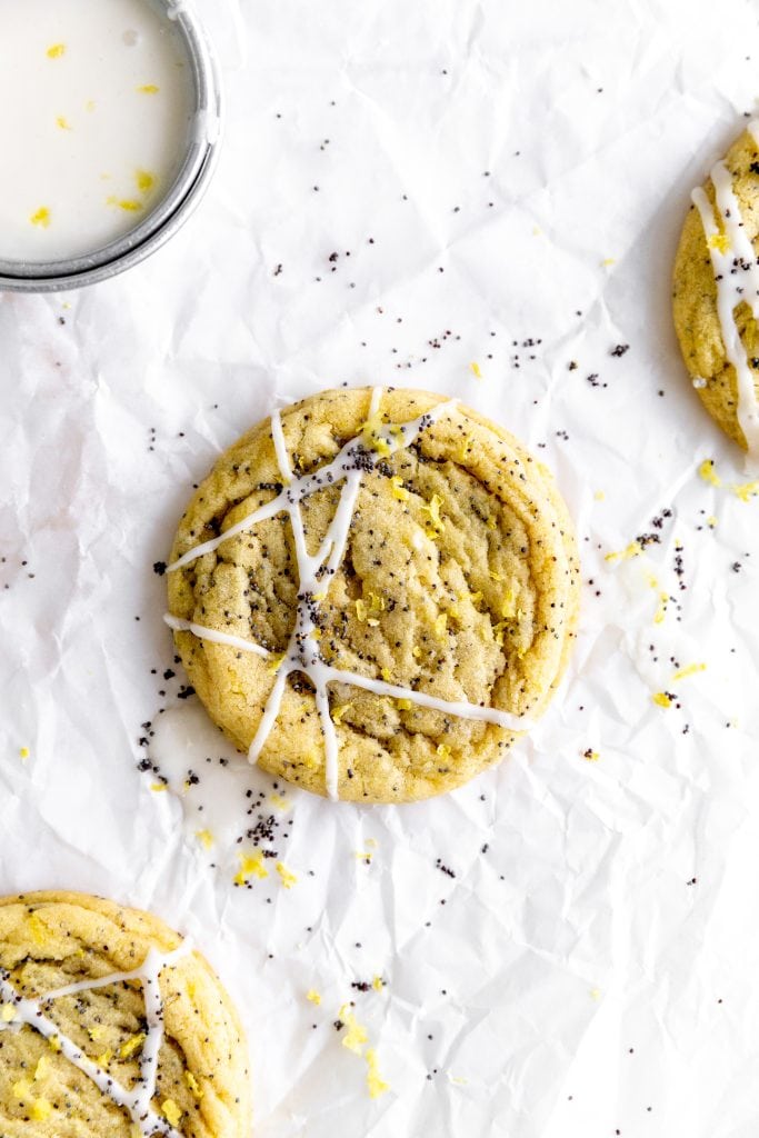 Lemon poppy seed cookies on parchment paper with a cup of lemon icing.