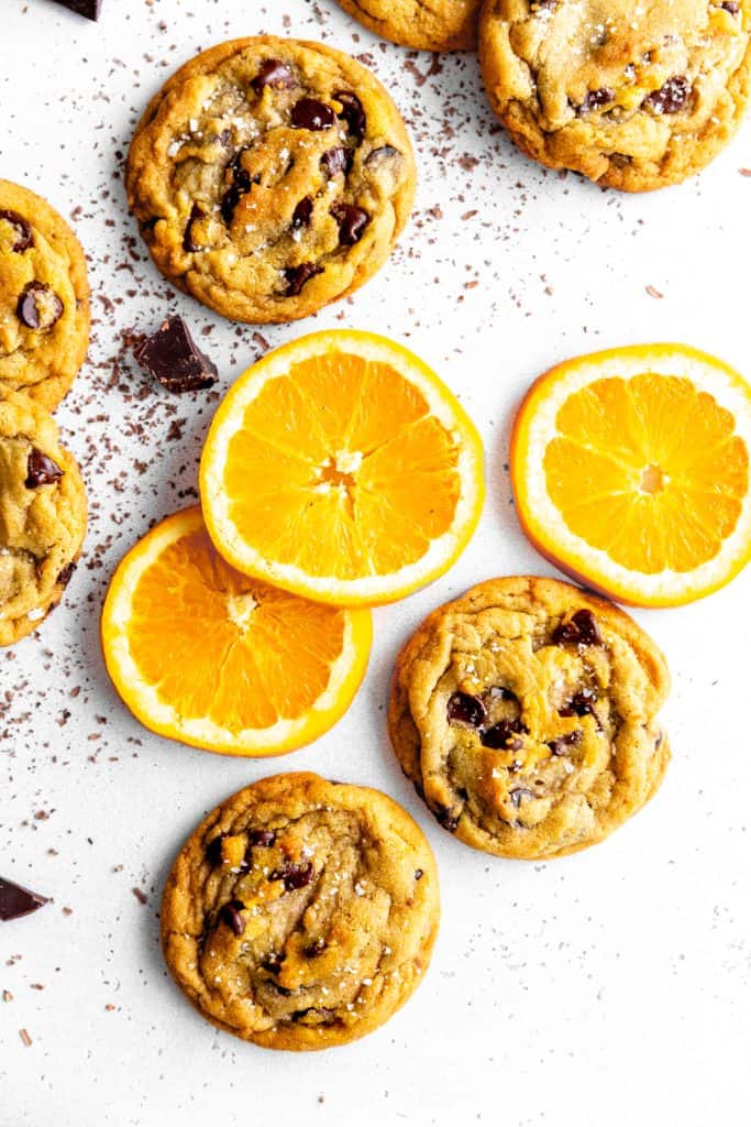 Orange chocolate chip cookies on a white surface with orange slices.