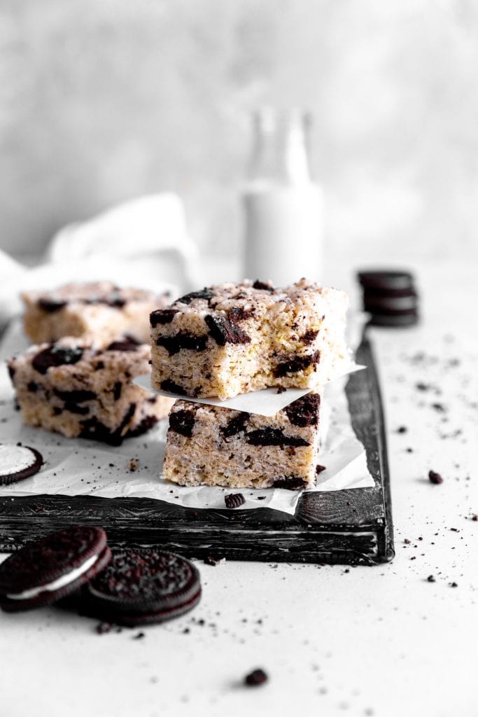 Oreo rice krispie treat with a bite taken out of it on top of another treat in front of a jug of milk.