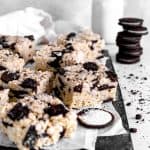 Oreo rice krispie treats on a baking sheet in front of a stack of oreos and a jug of milk.