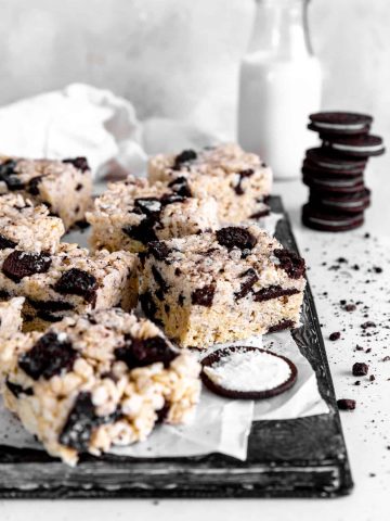 Oreo rice krispie treats on a baking sheet in front of a stack of oreos and a jug of milk.