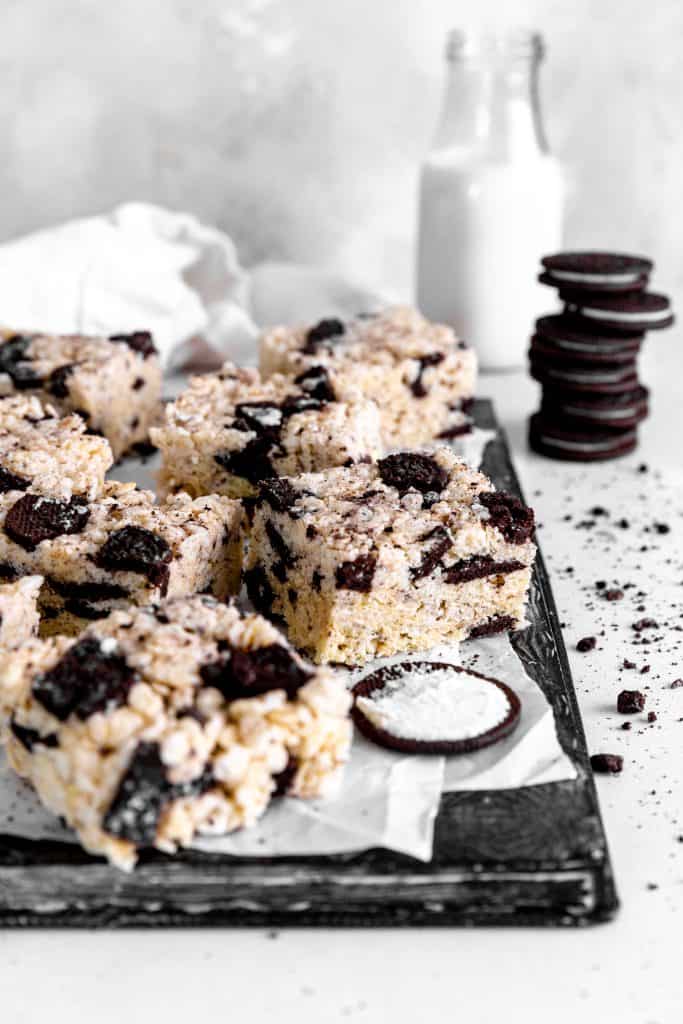 Oreo rice krispie treats on a baking sheet in front of a stack of oreos and a jug of milk.