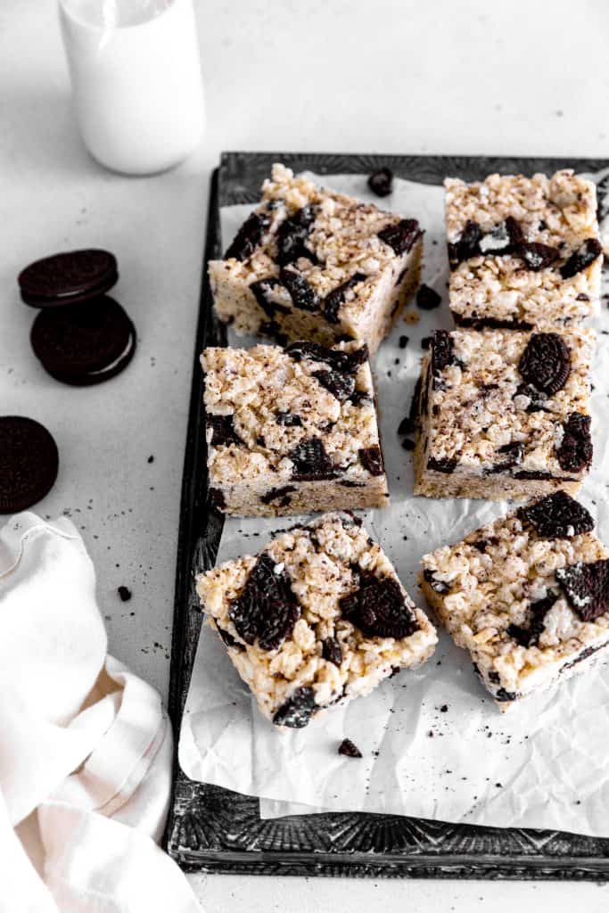 Oreo rice krispie treats on a baking sheet, scattered oreo cookies and a jug of milk.