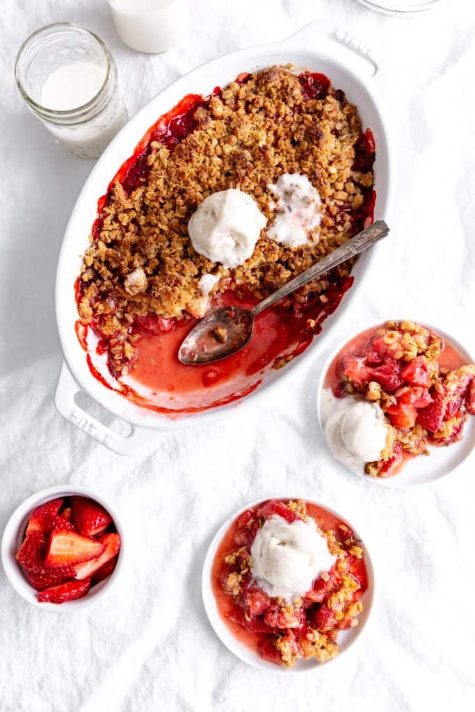 Baking dish of strawberry crisp and white plates with servings of the dessert.