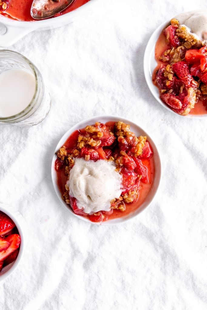 Two white plates with servings of strawberry crisp and a cup of milk.