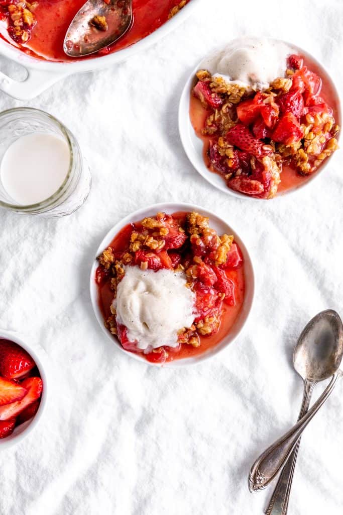 Two white plates with servings of strawberry crisp and a cup of milk.