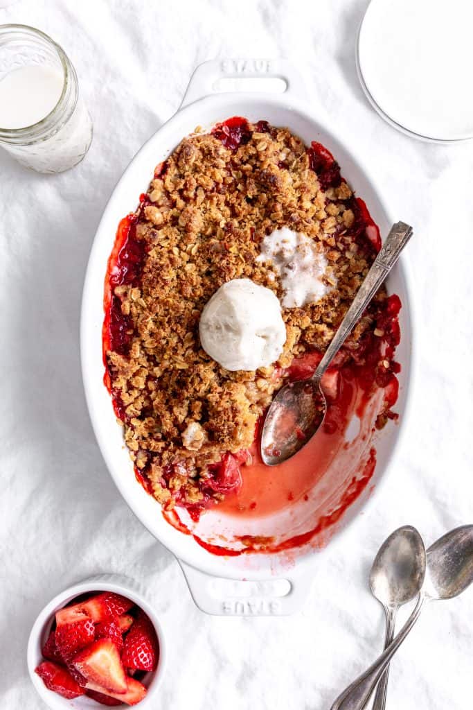 Silver spoon in a dish of strawberry crisp topped with vanilla ice cream.