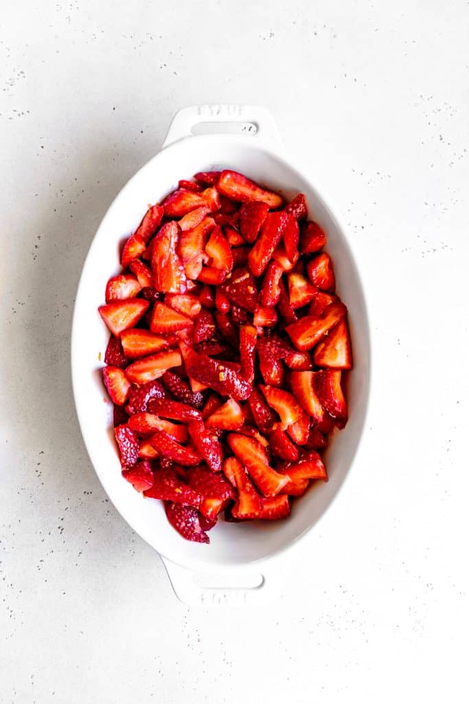 White baking dish filled with strawberry crisp filling.