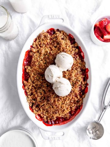 Baking dish of strawberry crisp topped with scoops of vanilla ice cream and a jug of milk.