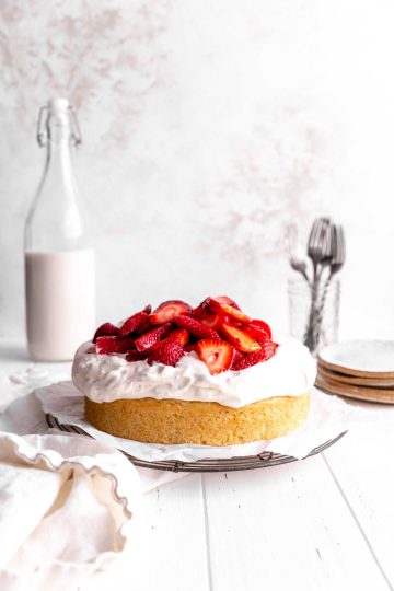 Strawberry shortcake cake topped with whipped cream and strawberries and a jug of milk.