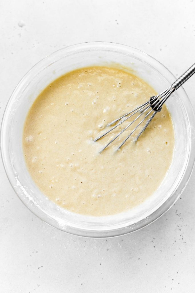 Vanilla cake batter in a glass bowl with a wire whisk.