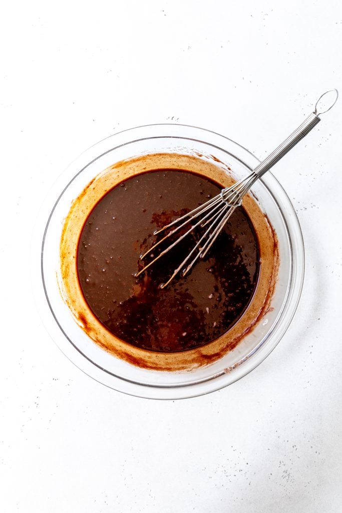 Glass bowl of melted chocolate and sugar with a wire whisk.