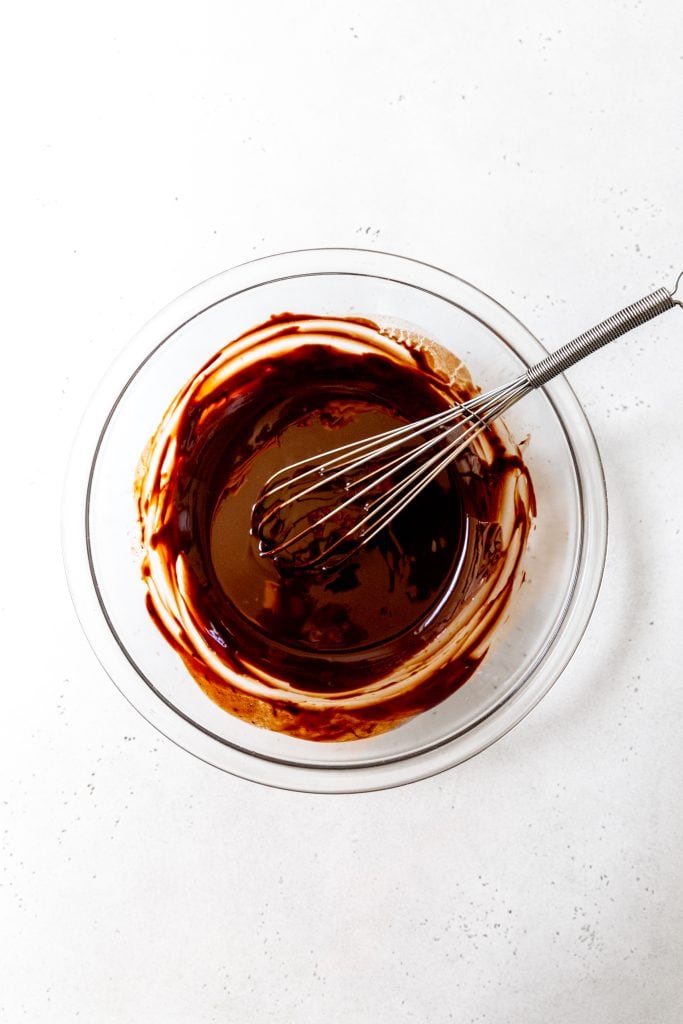 Glass bowl filled with melted chocolate and a whisk.