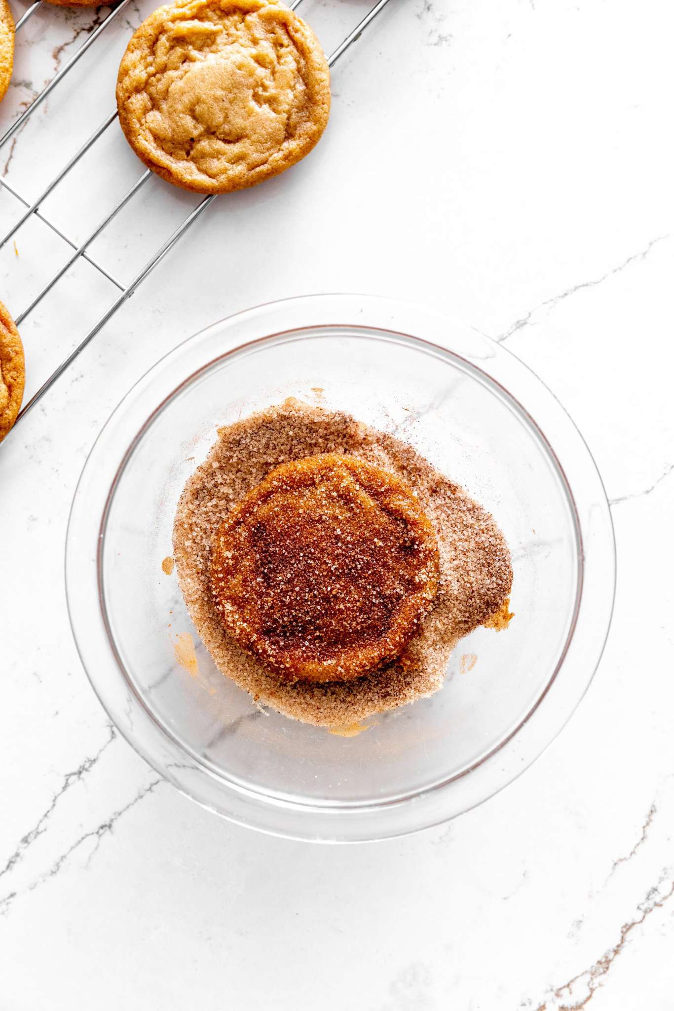 Apple cider cookie in a glass bowl of cinnamon sugar.