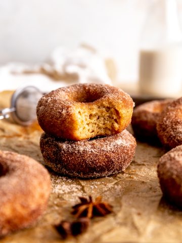 Apple cider donut with a bite taken out of it and a jug of milk.