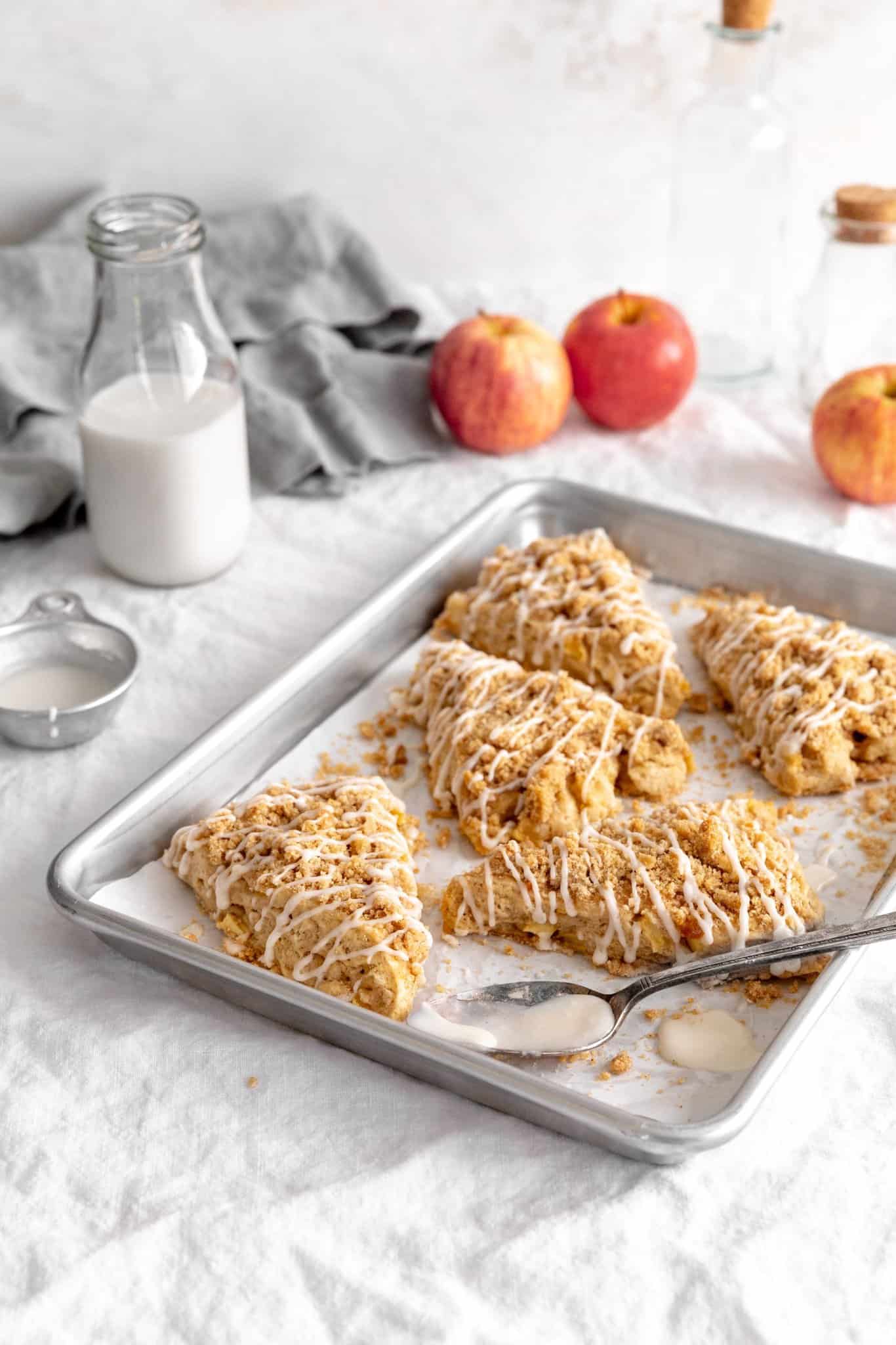 Apple cinnamon scones on a baking sheet, a jug of milk and a few apples.