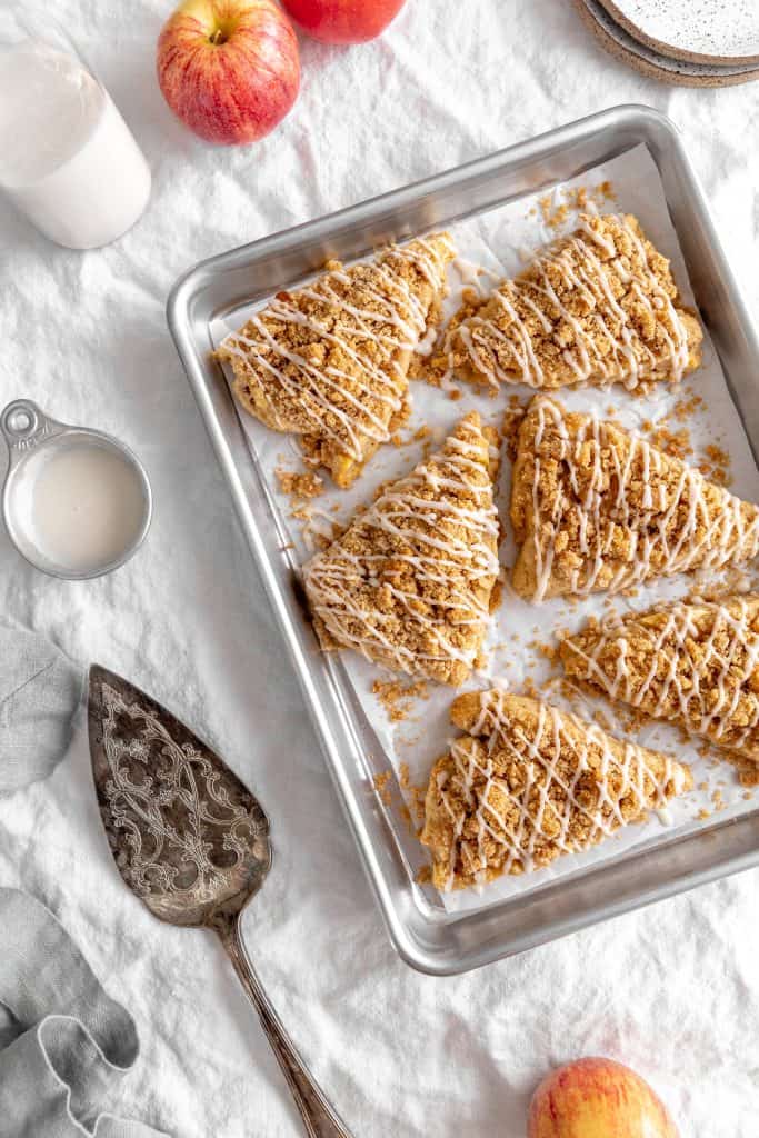 Apple cinnamon scones on a baking sheet, a jug of milk, plates and some apples.