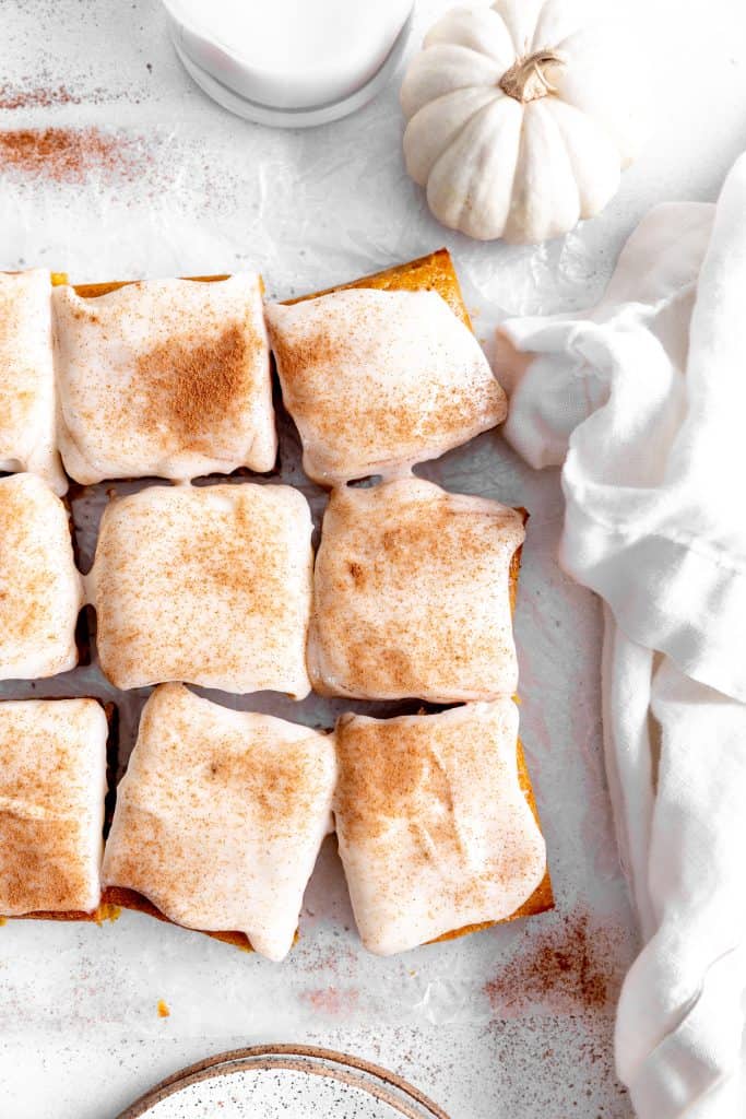 Frosted pumpkin bars, a glass of milk, a white pumpkin and a linen napkin.