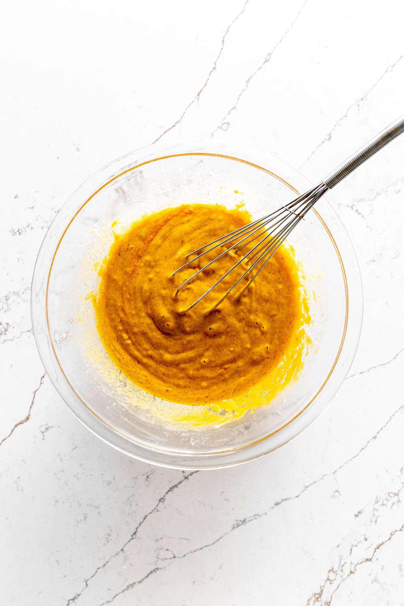 Glass bowl of pumpkin cake batter with a wire whisk.