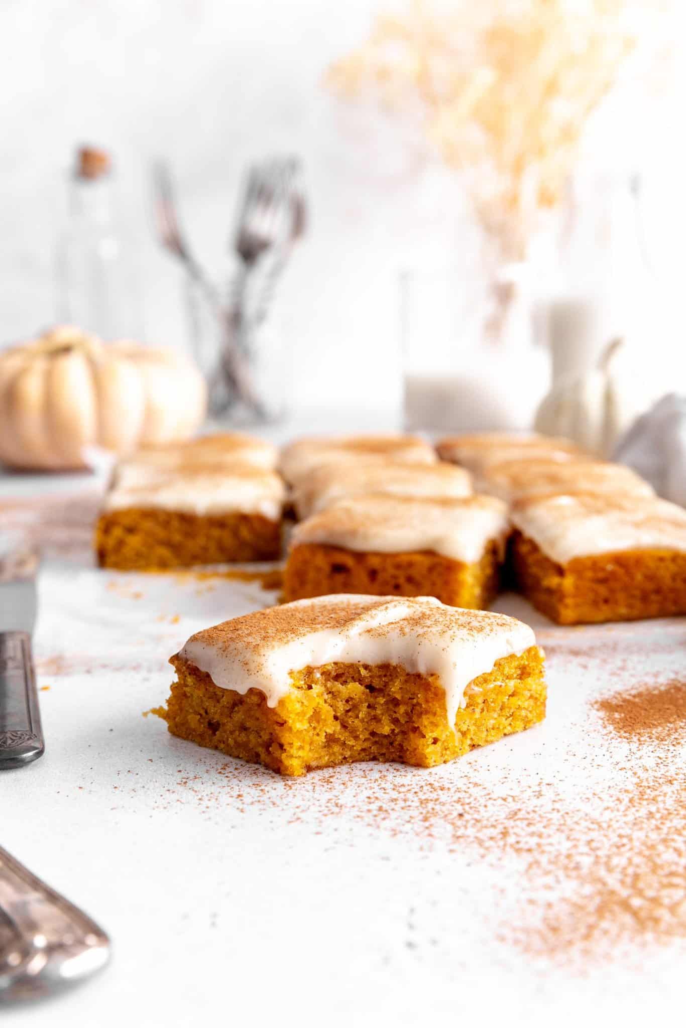 Pumpkin bar with a bite taken out, a jug of milk and a glass of flatware.