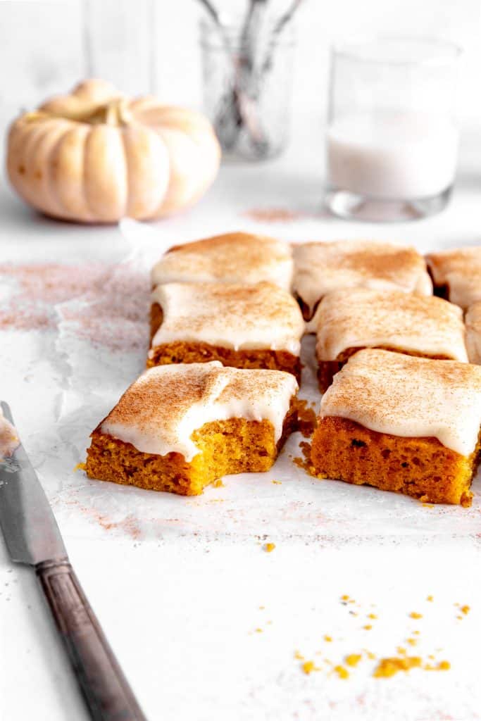 Pumpkin bar with a bite taken out, a jug of milk and a glass of flatware.