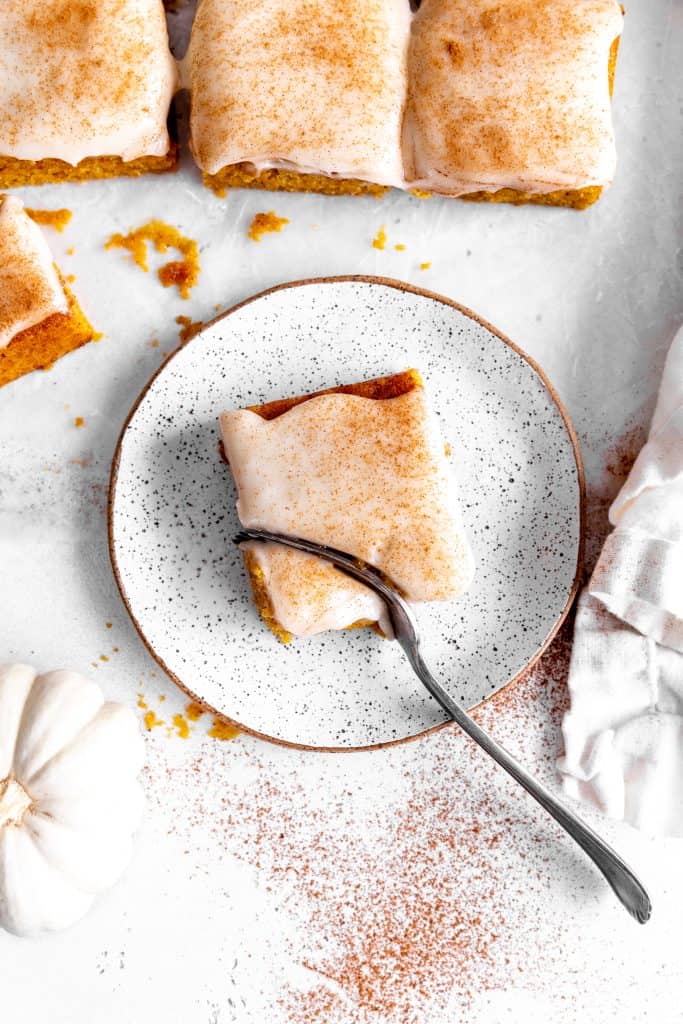 Fork cutting into a pumpkin bar on a white plate.